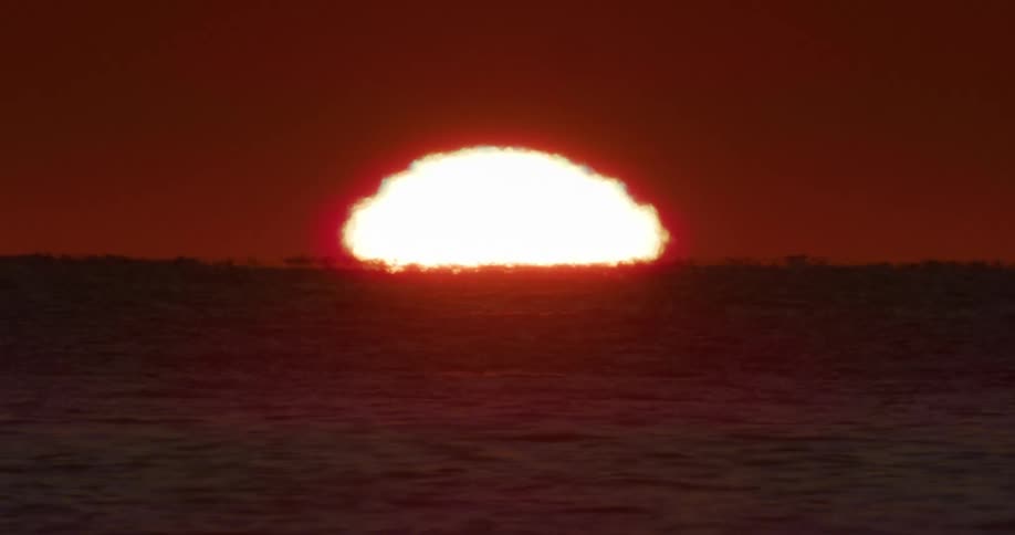 A large bright sun rising on the horizon over a body of water creating a vivid orange and red sky