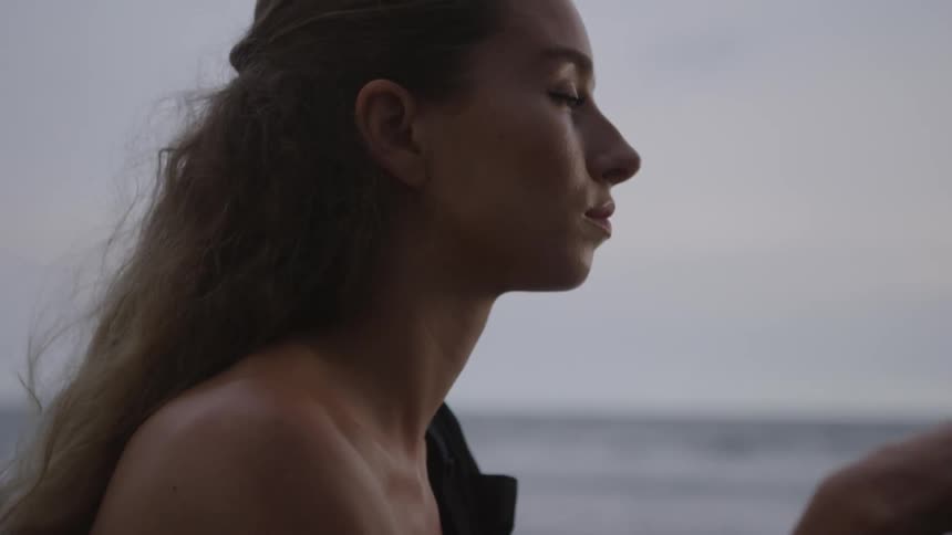 Side portrait of a young woman placing her hand on her face while sitting by the sea