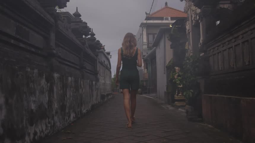 Blonde woman walking in a narrow corridor surrounded by old urban houses