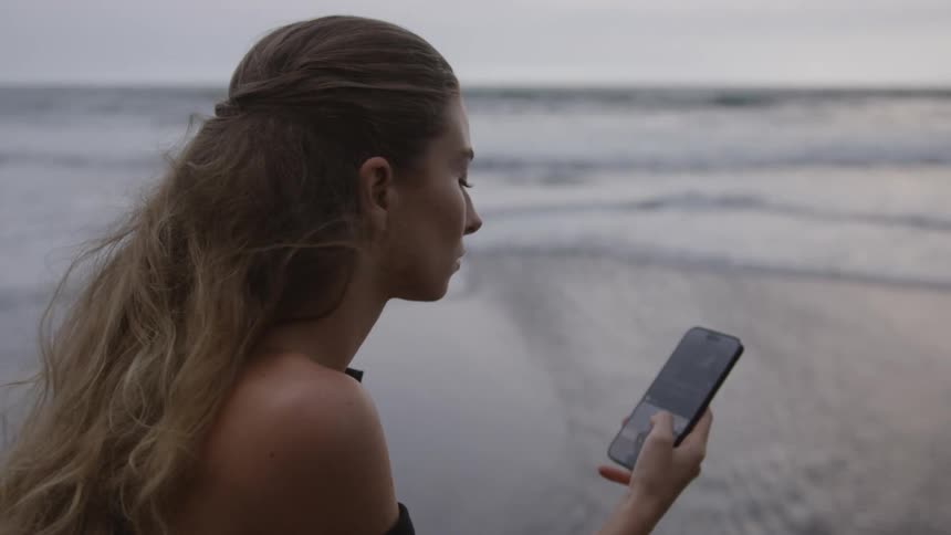 A woman at the beach is looking at photos on her phone