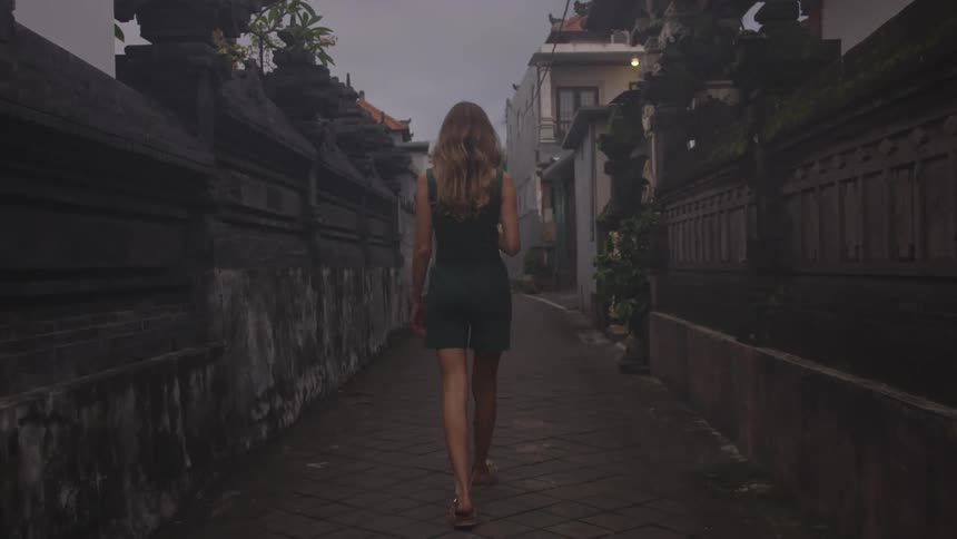 Blonde woman in back view walking on a narrow street through an urban neighborhood
