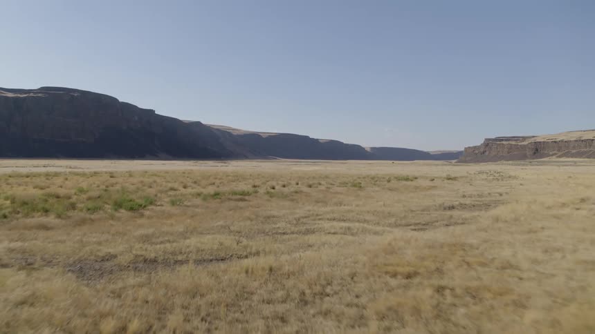 Low push over vast western plains with extensive dry grass and rocky cliffs in the distance