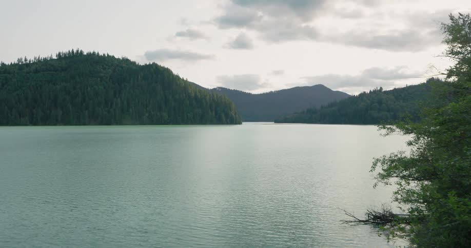 Reveal of a cyan colored glacial lake nestled between tree covered mountains