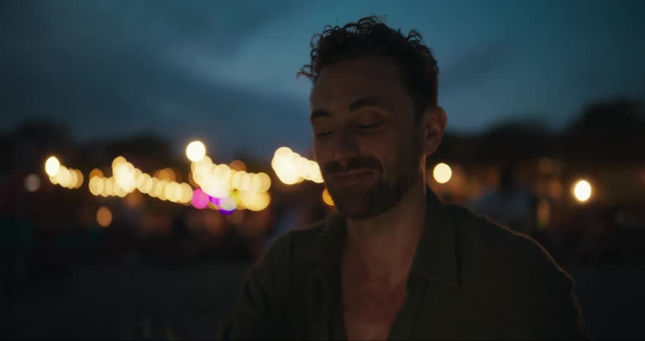 A young man talking on a smartphone with out of focus lights at evening or night time