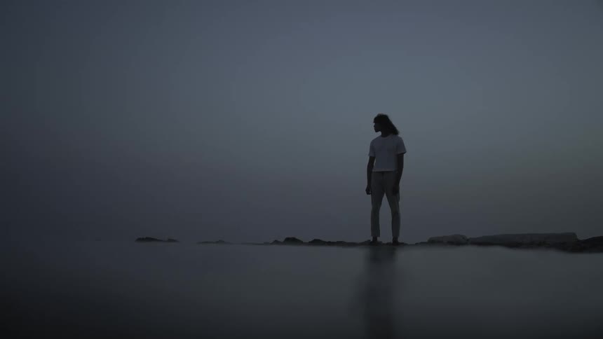 Silhouette of a man standing on a rock by the sea on a foggy day