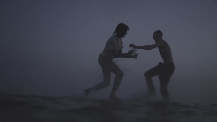 Two people running and playing in the waters of a lake on a cloudy day