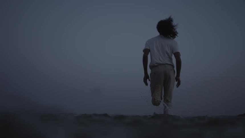 A young man running on the shallow water of a beach during twilight