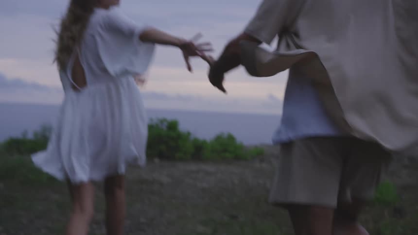 A man and woman run in nature with their arms stretched out to each other and lock hands