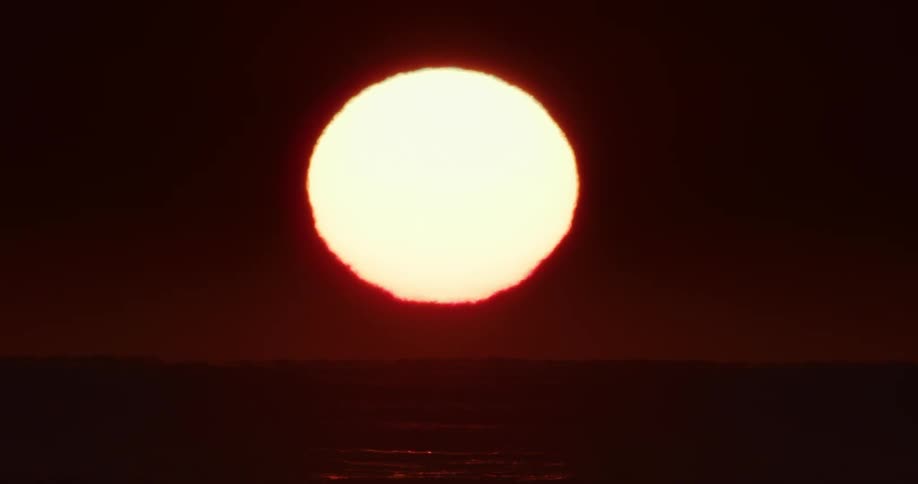 A large bright sun setting on the horizon with a deep red and orange glow against a darkening sky