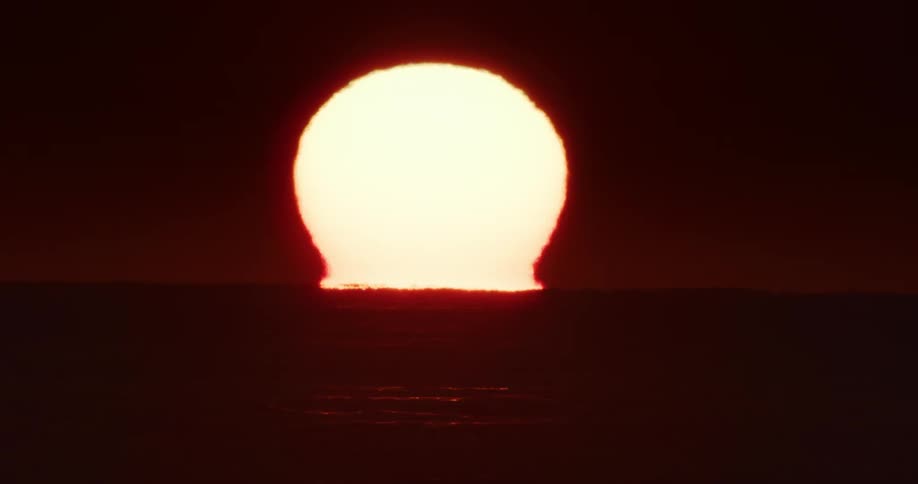 Sun rising on the horizon above the sea against a dark red sky