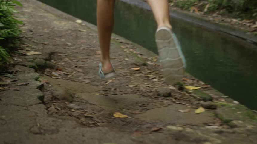 A woman in shorts and sandals runs along side the creek