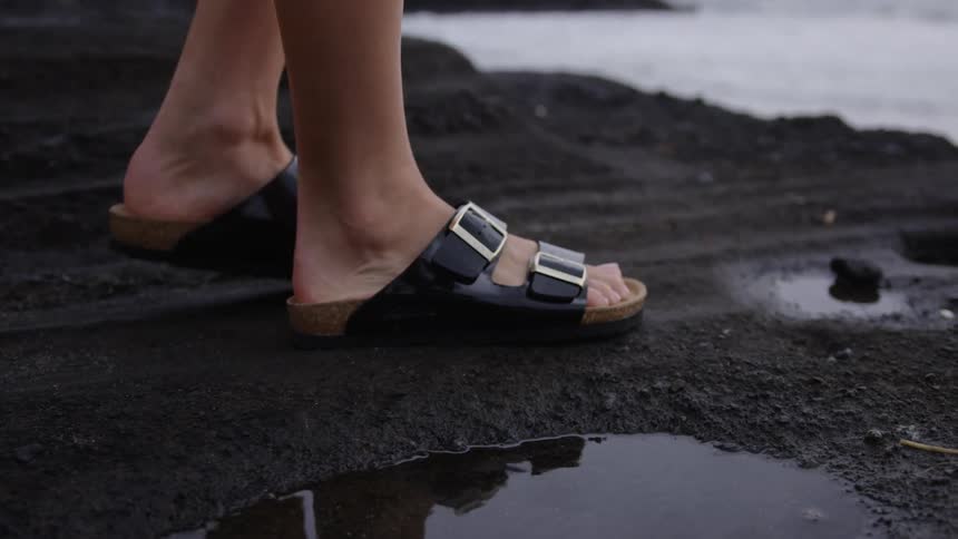 Feet of a person walking on black sand at the edge of a beach