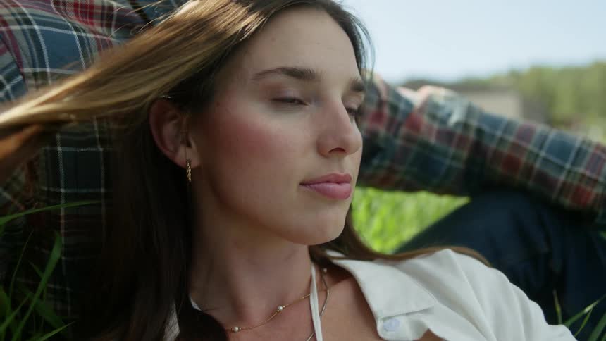 Portrait of a woman playing with her hair while sitting next to a man in a field