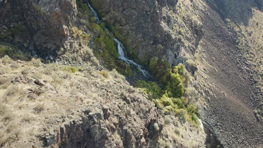 Reveal of a tall waterfall flowing down a rugged and steep desert cliff face