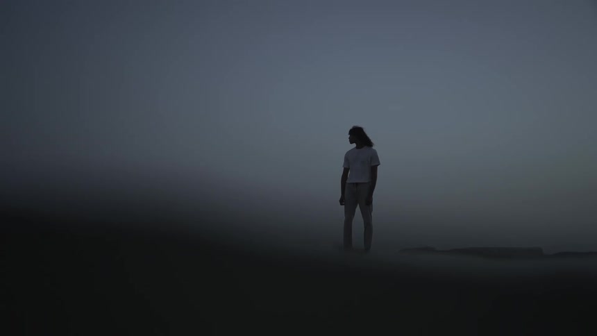 A solitary figure standing on the shore of a beach against a hazy overcast sky