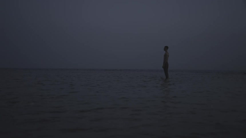 Silhouette of a man standing in shallow water during a dark cloudy day