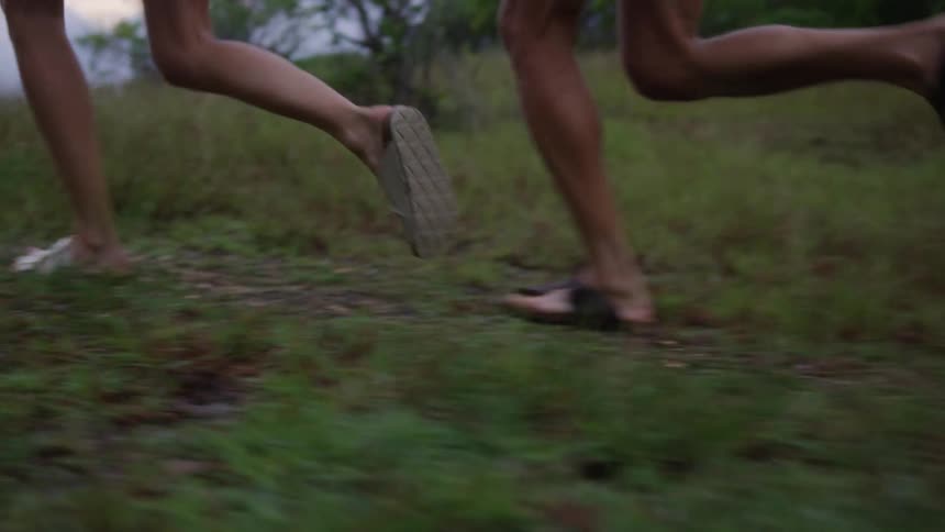 Legs of two people running on grass in a natural seaside setting