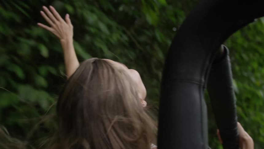 A young white woman leans out of jeep and extends her arm as she moves through a forest