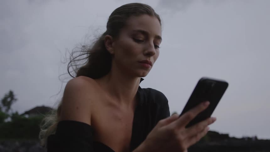 A woman is outside under cloudy skies using her smart phone