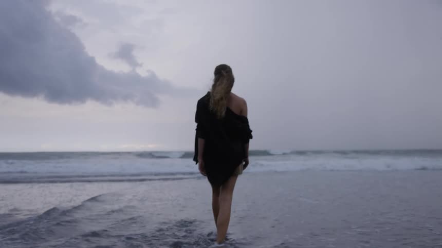 View of a woman from behind walking in the water on a beach and throwing a stone