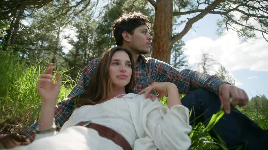 Woman lying on the chest of a man who is sitting in a field surrounded by vegetation