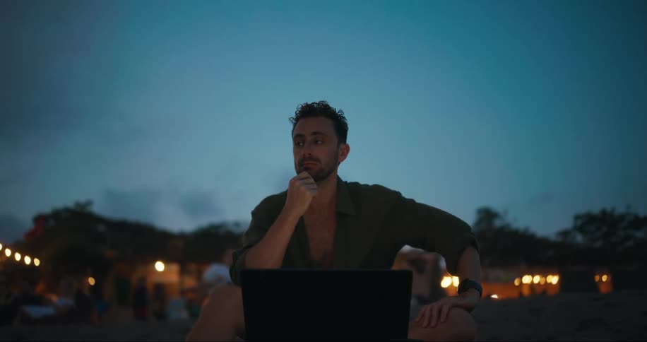 A man thinks as he uses his laptop on the beach