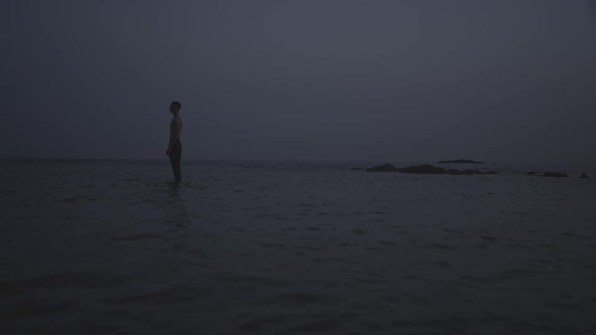 A man is standing in the water by the shore