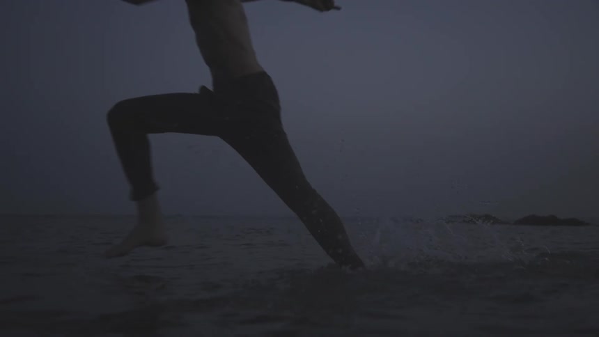 Two men run through the water on the shore