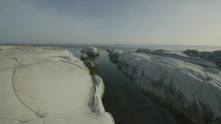 A serene coastal landscape with large smooth white rocks partially submerged in calm water