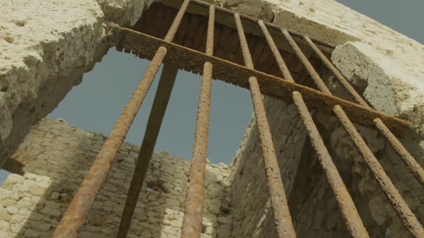 A closeup view of a rusted grate on the window of a broken and eroded concrete structure