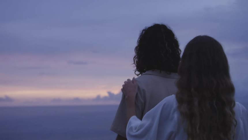 Rear view of a woman and a man walking in an elevated area by the sea with a panoramic view of a purple sky