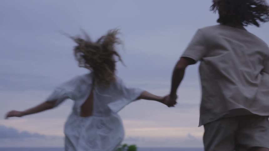 A man and a woman hold hands while running over open ground