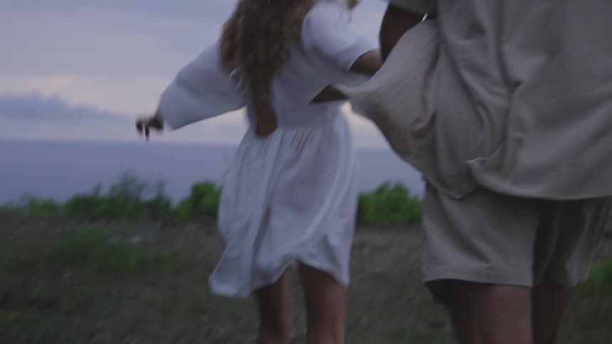Man and woman holding hands running towards a cliff by the sea