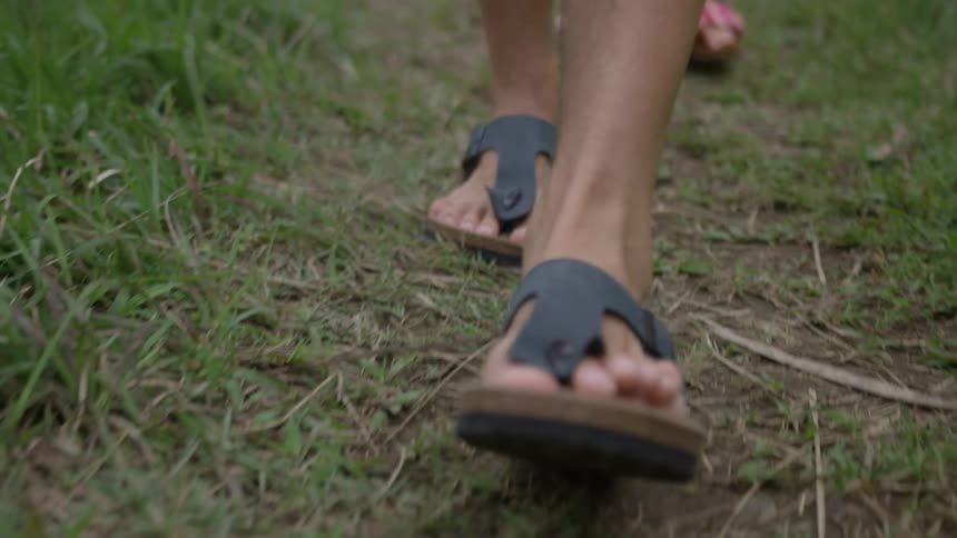 A man and woman in sandals walk in the grass