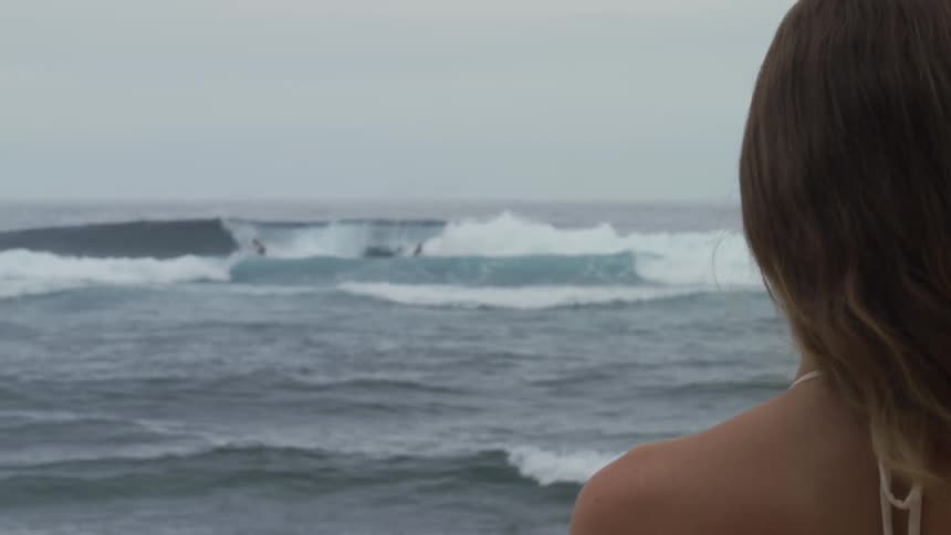 Back view of a woman looking out to sea with surfers