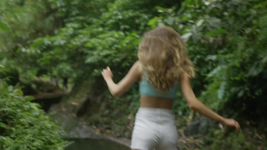 View of a woman from behind wearing white shorts walking in an environment surrounded by vegetation in a forest
