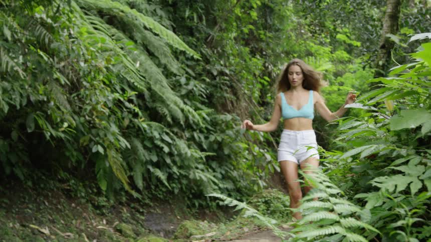 A teenage girl in shorts and a bikini top runs on a path in a forest