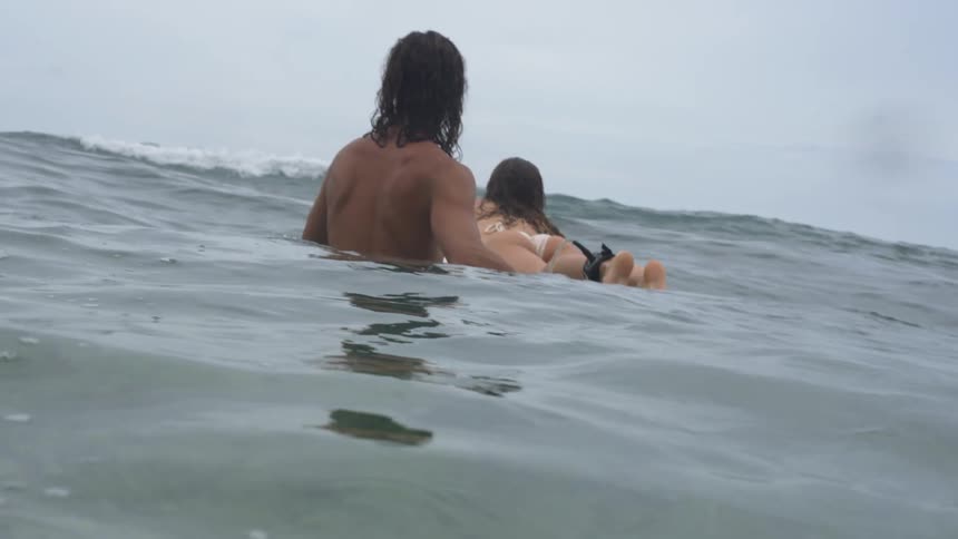 A man assists a woman paddling on a surfboard