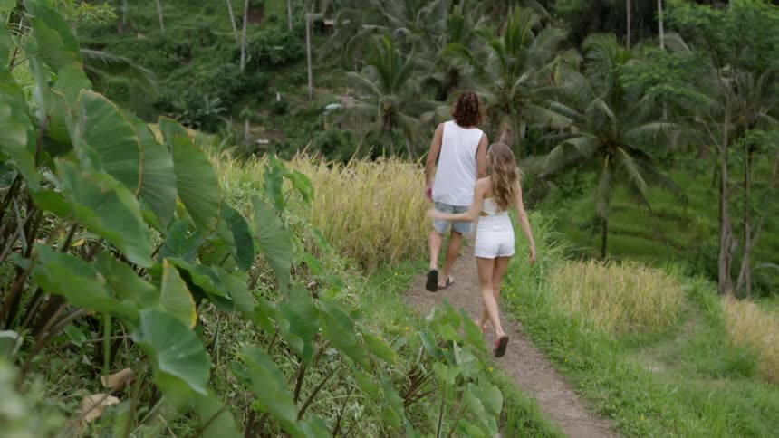 Man and woman walking on a hill in a natural environment with palm trees around