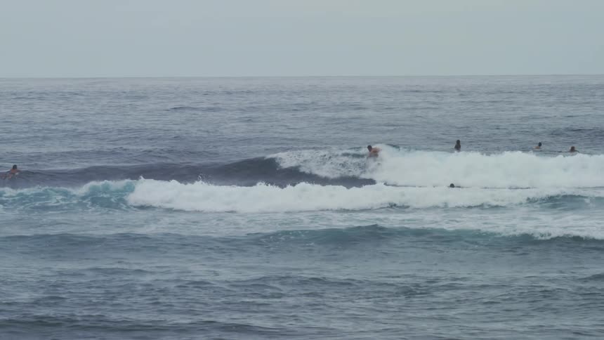 A surfer rides a wave on the ocean on an overcast day