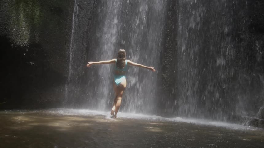 Woman with her back turned opening her arms towards the waterfall