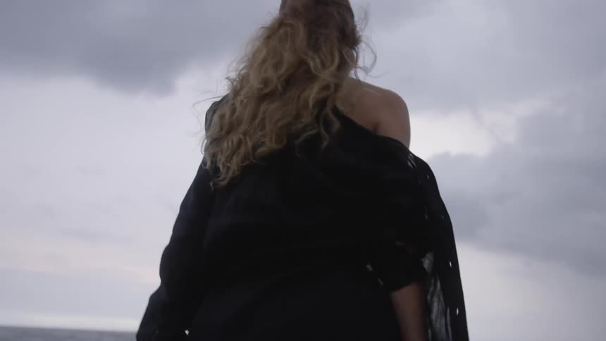 Close up of a woman browsing her smartphone sitting next to the shore of a beach at dusk