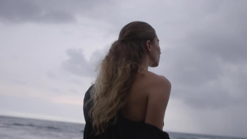 Woman sitting down using her smartphone and standing up walking along the beach