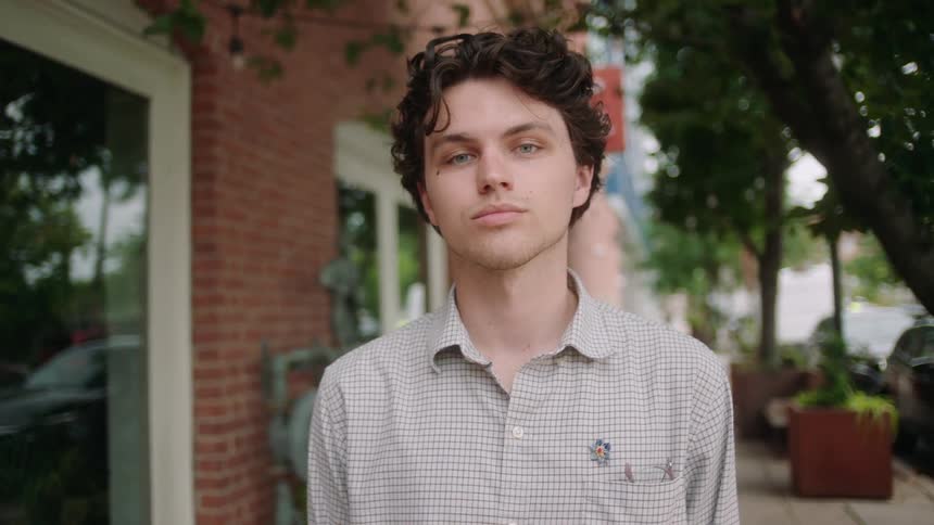 Close up of a young person standing on the sidewalk looking at the camera
