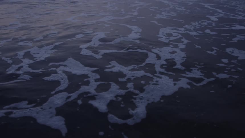Dark water with white foam patterns on the surface during twilight