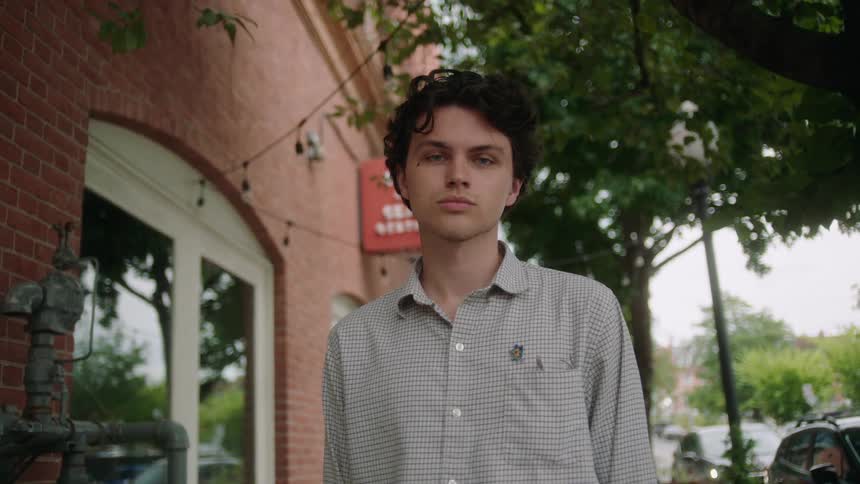 Close up of a person standing on the sidewalk looking at the camera