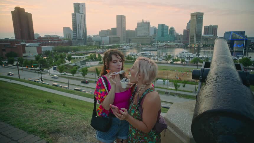 Friends playing with ice cream standing in front of a cannon overlooking a cityscape during dusk