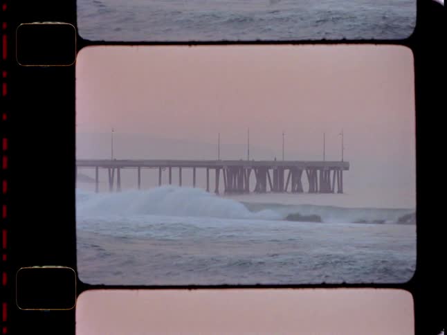Scene of strong waves with foam on the sea and in the background a dock and a reddish sky