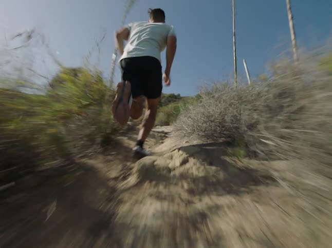 Back view of a man running fast down a mountain trail