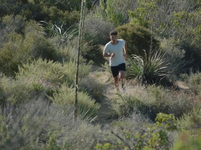 A person jogging on a dirt path or natural trail surrounded by shrubs